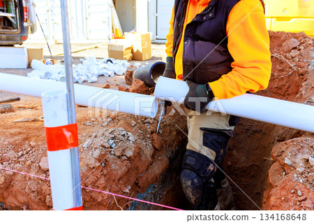 Construction worker installing pipes in trench at building site Construction worker installing pipes in trench at building site 134168648