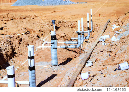 Construction site shows pipes fittings set in ground for plumbing work on new building 134168663