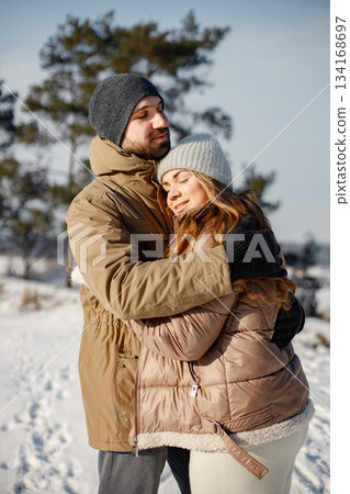 Portrait of romantic couple having fun on winter walk. Man and woman hugging. Family wearing warm jacket and knitted hats. 134168697