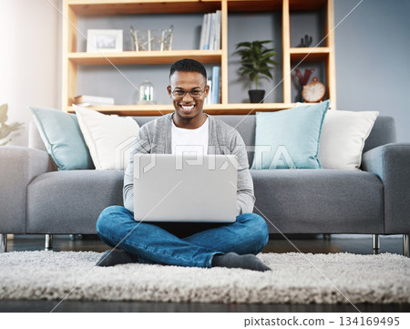 Computer, floor and portrait of man in home, online research and typing in living room for work or career opportunity. Happy, carpet and young african person working on laptop or technology in lounge 134169495