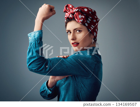 Flexing, strong and portrait of a pinup girl with muscle in studio for support, women power and fashion. Female person show bicep on grey background for motivation, freedom and retro or vintage style Flexing, strong and portrait of a pinup girl with muscle in studio for support, women power and fashion. Female person show bicep on grey background for motivation, freedom and retro or vintage style 134169507