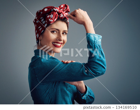 Strong, pinup girl and flexing muscle portrait of a woman in studio for beauty, power and fashion. Happy female person show bicep on grey background for motivation, freedom and retro or vintage style 134169510