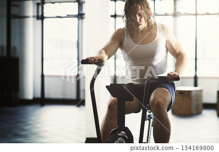 Fitness, elliptical and man training in gym, workout or exercise for strength, health or wellness. Sports fatigue, tired and exhausted male athlete exercising, cardio or cycling on cross trainer bike 134169800