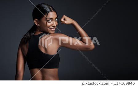 Portrait, smile and woman flexing back in studio isolated on a black background mockup. Strong flex, happy and Indian female athlete with bicep, arm strength or bodybuilder muscle, fitness or workout 134169940