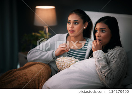 Popcorn, eating and people or friends with horror movies, scary show and sleepover on bed, streaming service or television. Gen z women relax in bedroom for drama TV film, home cinema or subscription 134170400