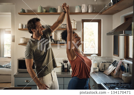 Interracial couple, happy and dance in kitchen for fun bonding, love or holiday together at home. Man and woman dancing in joyful happiness for relationship, romance or enjoying weekend in the house Interracial couple, happy and dance in kitchen for fun bonding, love or holiday together at home. Man and woman dancing in joyful happiness for relationship, romance or enjoying weekend in the house 134170471