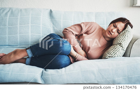 Woman, stomach ache or pain on home sofa with menstrual or period cramps in lounge. Sick, abdomen or colon problem of a female person with hands on tummy for constipation, digestion or virus 134170476