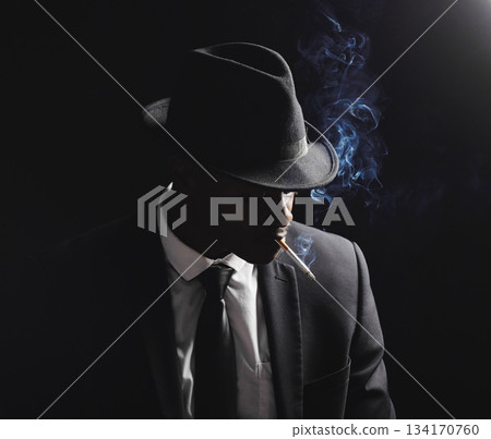 Man, gangster and cigarette in studio by black background with smoke, silhouette and dangerous in shadow. Mafia, secret agent or male in night for smoking with vintage aesthetic by dark backdrop Man, gangster and cigarette in studio by black background with smoke, silhouette and dangerous in shadow. Mafia, secret agent or male in night for smoking with vintage aesthetic by dark backdrop 134170760