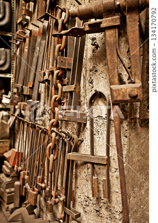 Steel, tools and workshop with blacksmith workplace and industrial factory wall background. Artisan, retro and metal tool for manufacturing, warehouse and brass forge industry equipment hanging Steel, tools and workshop with blacksmith workplace and industrial factory wall background. Artisan, retro and metal tool for manufacturing, warehouse and brass forge industry equipment hanging 134170792