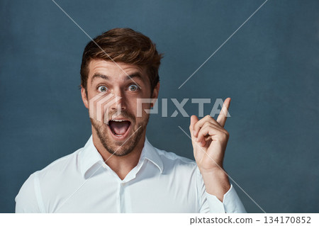 Portrait, wow and idea with a man pointing in studio on a blue background during a lightbulb moment. Face, surprise and eureka with an excited young male person looking shocked or amazed by good news 134170852