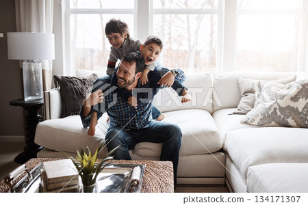 Father, boy children and playing in living room, fun and carefree with love, energy and happy at family home. Man play with kids on sofa, crazy and playful with piggyback and excited with laughter 134171307