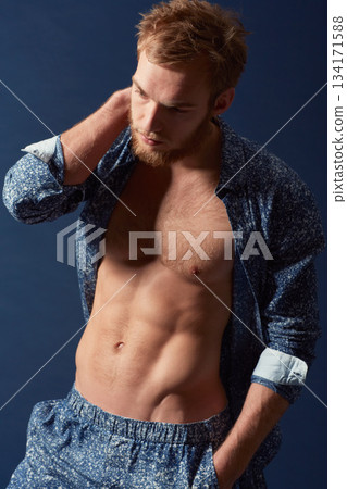 Fashion, body and muscle with a man in studio on a blue background wearing an open unbuttoned shirt. Fitness, chest and abs with a handsome young male model posing on a color wall for masculine style Fashion, body and muscle with a man in studio on a blue background wearing an open unbuttoned shirt. Fitness, chest and abs with a handsome young male model posing on a color wall for masculine style 134171588