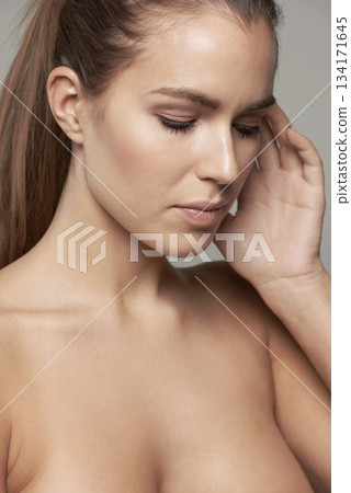 Touch, beauty and serious face of woman in studio for wellness, facial treatment and self care. Skincare, salon and female person with natural glowing skin, makeup and cosmetics on gray background 134171645