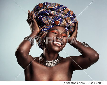 Beauty, black woman and laughing with African turban and smile in a studio. Isolated, grey background traditional makeup with a young female model with culture crown and fashion with cosmetics Beauty, black woman and laughing with African turban and smile in a studio. Isolated, grey background traditional makeup with a young female model with culture crown and fashion with cosmetics 134172046