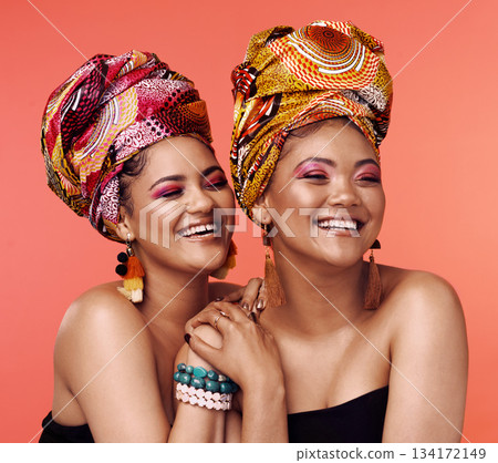 African fashion, friends and women laugh on orange background with cosmetics, makeup and accessories. Glamour, luxury and face of female people with exotic jewelry, traditional style and head scarf African fashion, friends and women laugh on orange background with cosmetics, makeup and accessories. Glamour, luxury and face of female people with exotic jewelry, traditional style and head scarf 134172149