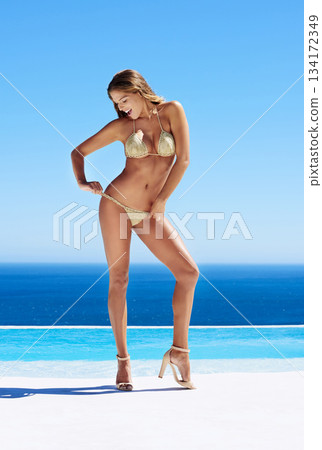Happy, young woman in bikini and heels at seashore in blue sky. Summer vacation or holiday, confidence and cheerful female model at sea or beach for fun or healthy body in stylish swimwear Happy, young woman in bikini and heels at seashore in blue sky. Summer vacation or holiday, confidence and cheerful female model at sea or beach for fun or healthy body in stylish swimwear 134172349