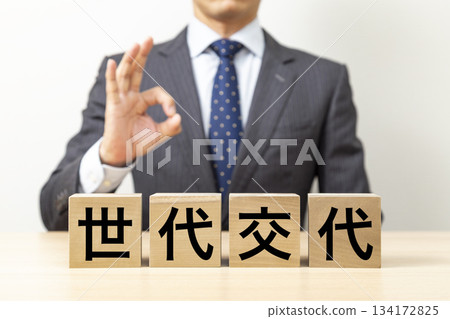 一位商人擺出「OK」的姿勢,旁邊立著一塊寫著「世代更迭」的積木。 一位商人擺出「OK」的姿勢,旁邊立著一塊寫著「世代更迭」的積木。 134172825
