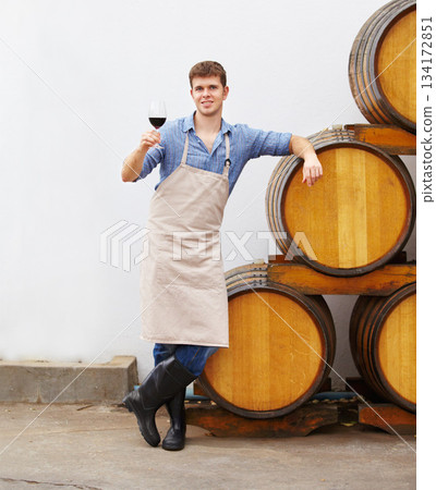Portrait, wine and oak barrels with a man holding a glass in a winery or distillery as an artisan and sommelier. Drink, red blend and alcohol with a male beverage maker in a factory or warehouse Portrait, wine and oak barrels with a man holding a glass in a winery or distillery as an artisan and sommelier. Drink, red blend and alcohol with a male beverage maker in a factory or warehouse 134172851