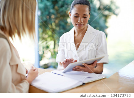 Woman, tablet and reception at spa for beauty appointment, booking or check in at the resort. Female talking to receptionist or beautician at counter on technology for salon reservation or treatment Woman, tablet and reception at spa for beauty appointment, booking or check in at the resort. Female talking to receptionist or beautician at counter on technology for salon reservation or treatment 134173753