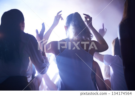 Concert, music festival and women from back, lighting and energy in crowd at live night event. Dance, fun and group of excited fans in arena at rock band performance or audience at techno rave party. 134174564