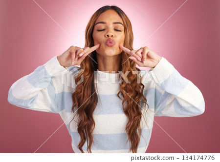 Fingers on face, comic and a woman in studio on a gradient pink background feeling silly, cute or goofy. Dimples of young female fashion model looking playful for fun with hands on cheek for kiss 134174776