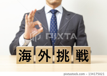 一位商人擺出「OK」的姿勢，旁邊立著一塊寫著「海外挑戰」的積木。 134175021