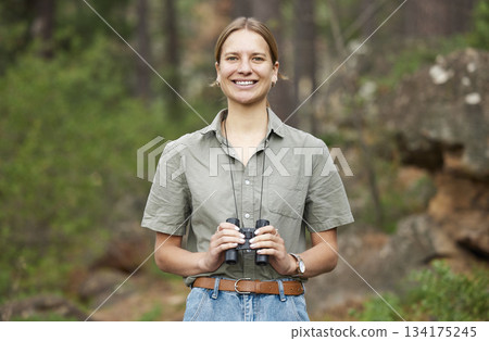 Binocular, forest and portrait of happy woman hiking for nature journey, jungle adventure and travel in outdoor explore. Face of a young person birdwatching and trekking in eco friendly green woods 134175245