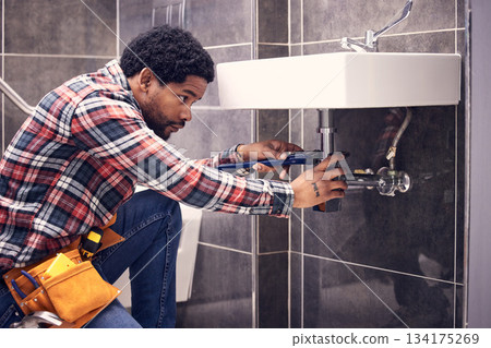 Black man, plumber and maintenance in bathroom, fixing sink pipe with wrench and plumbing industry. Manual labor, male with focus and trade, handyman doing repairs with tools on home renovation 134175269