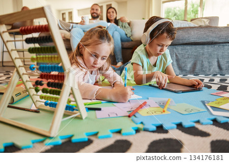 Floor, learning and children with parents relax on sofa for education, creative writing and online digital games at home. Kids on carpet with tablet, headphones and stationery with family on couch 134176181