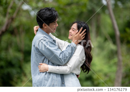 Young asian couple hugging as a man holding or touching woman's face while standing outdoors in park Young asian couple hugging as a man holding or touching woman's face while standing outdoors in park 134176279