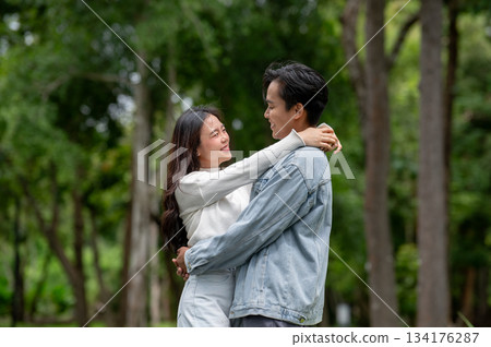 Young asian couple of man and woman holding and hugging each other while standing outdoors in park. 134176287