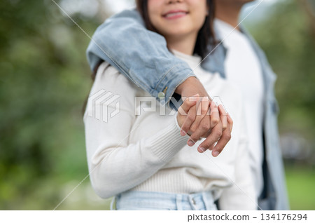 Close up of young couple holding hands lacing fingers while standing or walking outdoors in the park 134176294