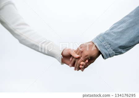 Close up of a young couple holding hands standing outdoors under bright sky or white background. 134176295