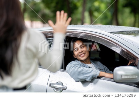 Happy young asian man putting arm out of car window with raindrops on roof as waiting for girlfriend 134176299