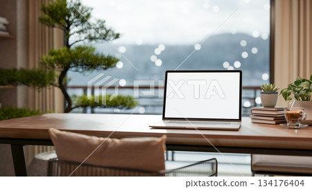 Blank screen laptop with books and coffee on wooden table across bonsai tree and snow outside balcony. 134176404