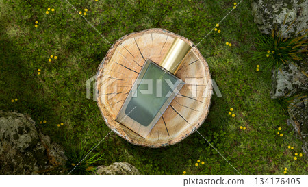 Luxury glass bottle beauty spray perfume on tree stump log in grass lawn garden with moss cover rock 134176405