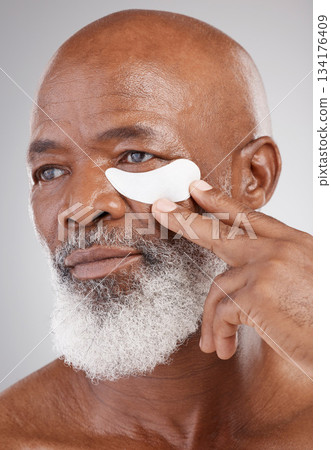 Skin care, collagen eye mask and black man with hand on face on studio background for professional anti ageing spa treatment. Dermatology, cosmetic process and mature model with skincare on eyes. Skin care, collagen eye mask and black man with hand on face on studio background for professional anti ageing spa treatment. Dermatology, cosmetic process and mature model with skincare on eyes. 134176409