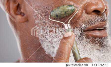 Face roller, closeup and senior man with skincare, stone and dermatology product for skin glow. Elderly, cheek and facial roll of African male model doing self care for grooming with jade for beauty Face roller, closeup and senior man with skincare, stone and dermatology product for skin glow. Elderly, cheek and facial roll of African male model doing self care for grooming with jade for beauty 134176459