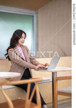 Young asian woman looking and typing on laptop sitting on sofa bench at table in cafe or coffee shop Young asian woman looking and typing on laptop sitting on sofa bench at table in cafe or coffee shop 134176876