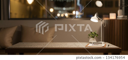 Calculator over clipboard with pot plant and lamp on marble table across sofa and window in dim room 134176954