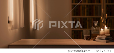 Alcohol bottle and glass cup with candles over book on wooden table across bookshelf in dim lit room 134176955