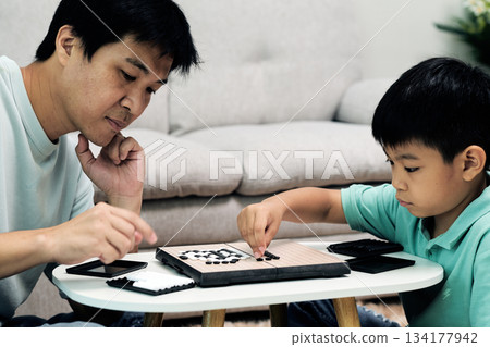 Child placing Go stone during thoughtful match with father at home; strategic thinking, focus and meaningful family interaction through educational board game activity 134177942