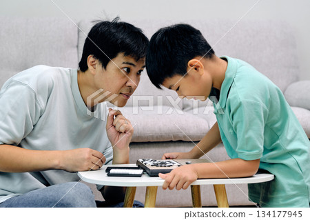 father and child leaning in closely during a Go match, showing focus, strategy, and playful family interaction in an educational indoor activity that encourages thinking and bonding father and child leaning in closely during a Go match, showing focus, strategy, and playful family interaction in an educational indoor activity that encourages thinking and bonding 134177945