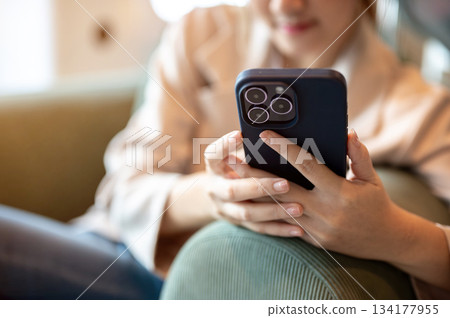 Close up of woman looking at smartphone while sitting leaning on green sofa or armchair in the cafe. 134177955