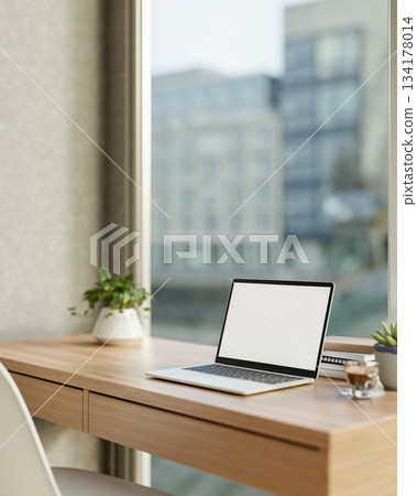 White screen laptop and coffee aside potted plant on wooden desk with cityscape outside glass wall. 134178014