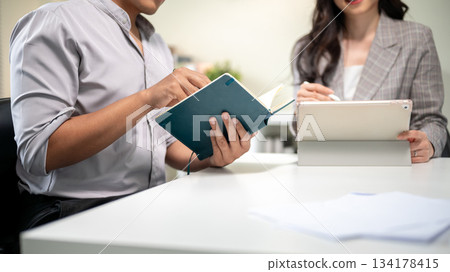 Close up businessman holding notebook aside woman coworker holding tablet at working table in office Close up businessman holding notebook aside woman coworker holding tablet at working table in office 134178415