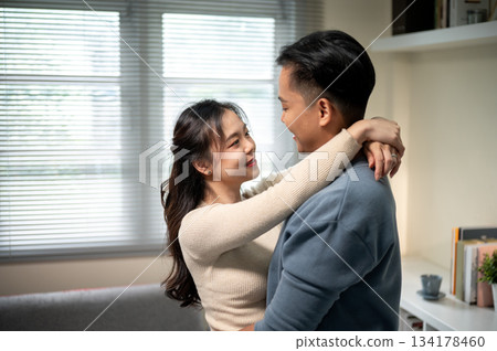 Sweet couple locking eyes asian woman with hands holding hugging man's neck standing in living room. 134178460