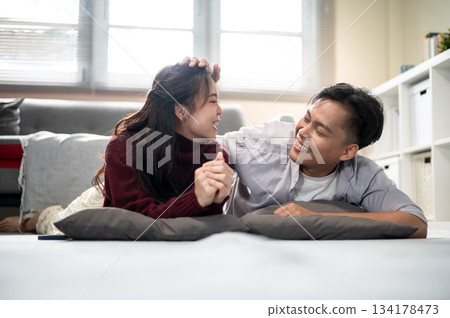 Asian man holding or touching woman's head while lying together over cushion on living room's floor. Asian man holding or touching woman's head while lying together over cushion on living room's floor. 134178473