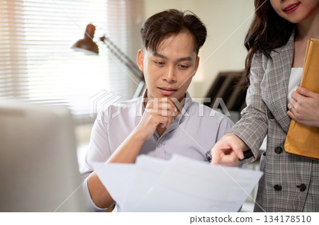 Asian businessman looking at document as woman coworker pointing on paper at working table in office 134178510