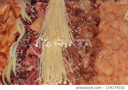Assortment of raw marinated meats including beef, chicken, rice cakes, and enoki mushrooms prepared for Asian BBQ cooking. Assortment of raw marinated meats including beef, chicken, rice cakes, and enoki mushrooms prepared for Asian BBQ cooking. 134179102
